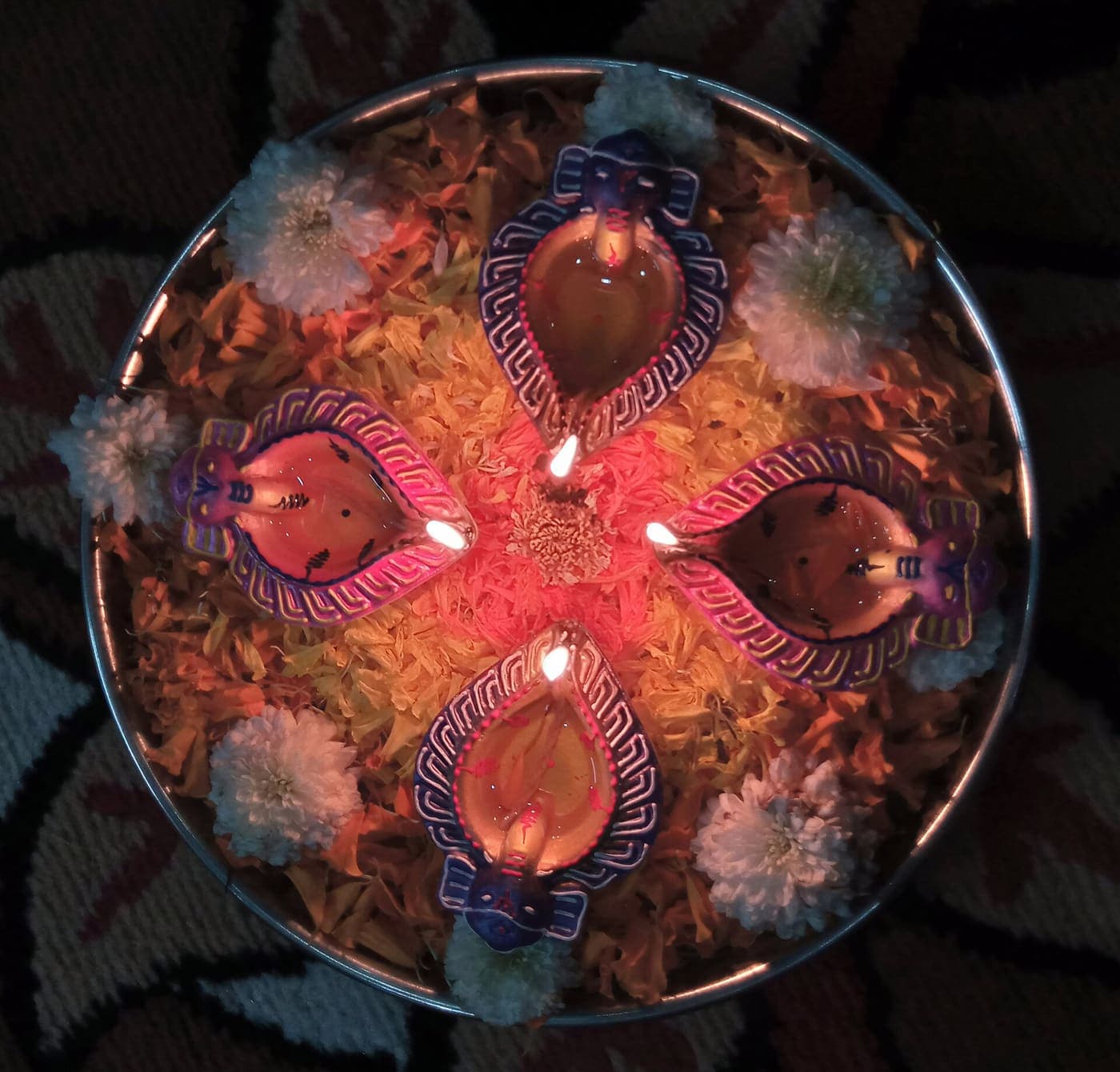 Four painted clay diyas on a plate of marigold petals